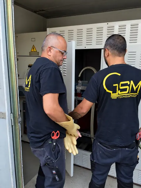 Due tecnici in maglia G.S.M., coi guanti isolanti, davanti alla cella di media tensione di una cabina